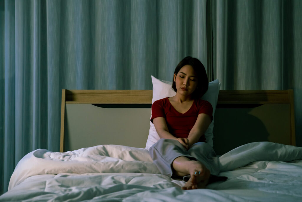 Depressed young beautiful asian woman sitting alone on bed at night. Stressed insomnia woman girl thinking of her problem with sadness and negative emotion. Mental health, healthcare and social issue concept.